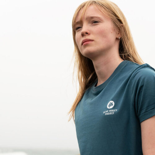 Female model wearing a sustainable T-shirt made from organic cotton and seaweed blend, featuring a sea turtle design on the back. Proceeds from sales support sea turtle conservation. Image.